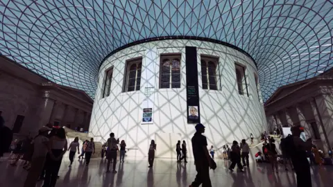 The courtyard at the British Museum, covered in glass, with visitors walking around 