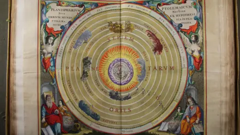 An elaborate and colourful double page illustration of planets in a circular pattern, with Latin descriptions and depictions of biblical and celestial figures in the corners.