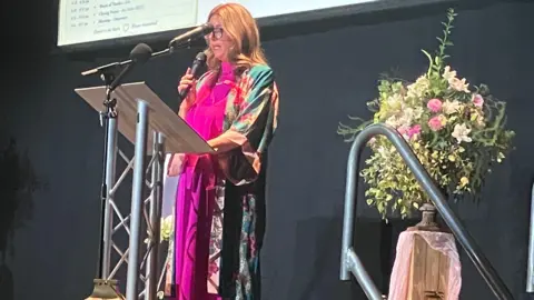 Sam Read/BBC Woman on a stage in front of a lectern She wear brightly coloured kimono over a vivid pink dress and speak to the 