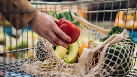 Close-up shot of female hand putting a red bell pepper into a mesh grocery bag.