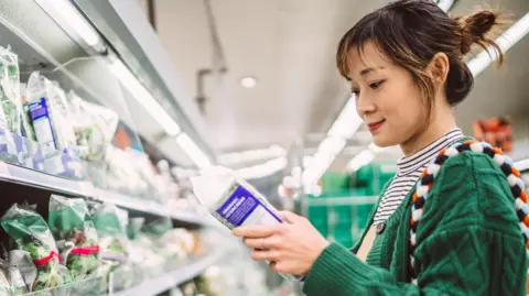 Getty Young woman inspects the packaging of a food item in a supermarket aisle