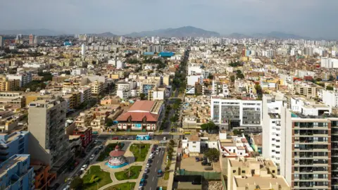 Alexandre Morin-Laprise/Getty Images Lima, Peru, with many buildings in the foreground and mountains in the background under a grey sky