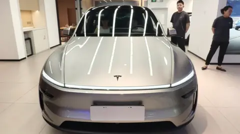 Future Publishing via Getty Images) Two people looking at a silver Tesla Model Y L electric vehicle in a showroom in Shanghai, China.