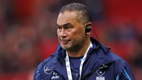 Bristol Bears director of rugby Pat Lam stands wearing a blue jacket and also has an ear piece in during a warm-up for a Prem Rugby match.