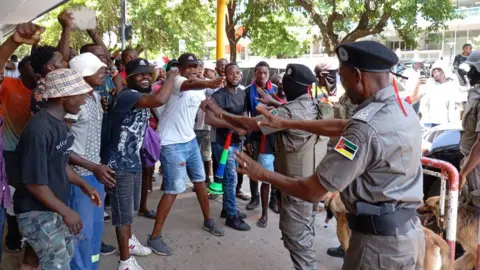 AFP A group of protesters passionately gesture at two uniformed police officers on streets of Maputo