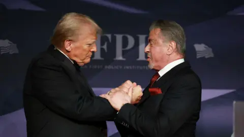 Donald Trump and Sylvester Stallone clasp each other's hands on stage at a gala at Mar-a-Lago in November 2024 