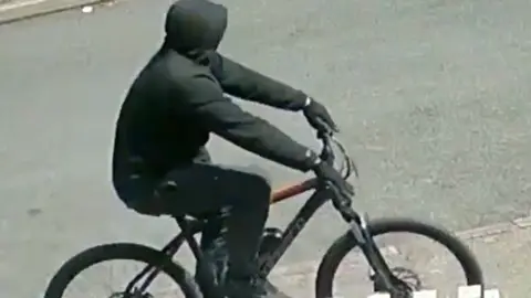 West Midlands Police Another image of a man dressed completely in black, riding a black bicycle in front of a white fence