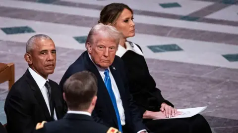 Getty Images Melania Trump sits next to her husband Donald Trump and former President Barack Obama