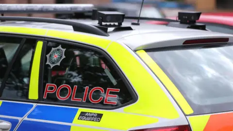 A marked blue and yellow police car. The photo is cropped so it is just the back window of the car.