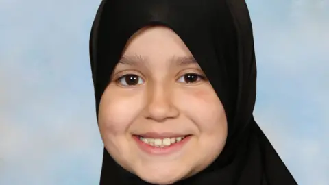 Surrey Police Sara Sharif wearing a black head scarf. She is smiling at the camera