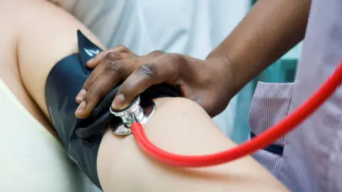 GETTY IMAGES Checking pulse in hospital. An arm is outstretched as a nurse checks the patients blood pressure. 