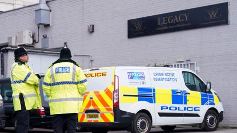 Two police officers standing in front of a van looking up at Legacy sign on building wall