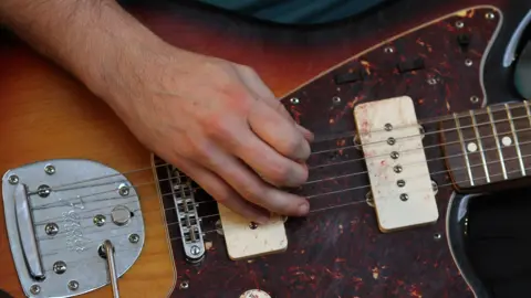 An anonymous hand plays a guitar on stage.