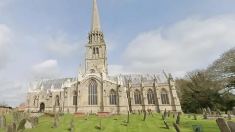 The church is an unusal shape. The bell tower and steeple are in the middle of the church which has an entrace at one end and large stained glass windows underneath the tower. 