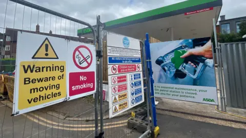 An Asda petrol forecourt which has been fenced off. There are Thames Water danger and warning signs on the metal fence. 