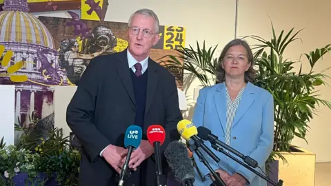 Man and woman standing speaking at microphones 