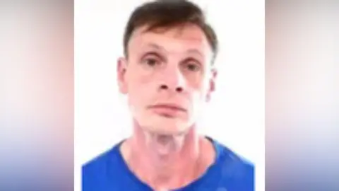 Cleveland Police A mugshot of John Laidlaw. He has short brown hair with a side parting and brown eyes. He is wearing a blue top and looking at the camera with a serious expression.