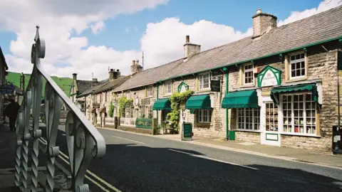Derbyshire County Council A street view of Castleton village. There are victorian-era shops pictured on a sunny day. 