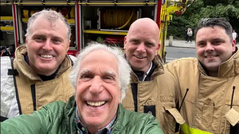 Selfie of Henry Winkler surrounded by three firefighters