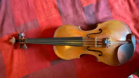 The brown, wooden violin lying on a patterned red fabric. 