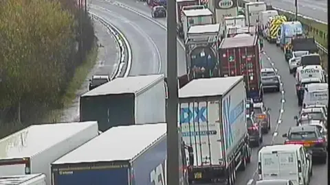 Image showing cars and HGVs queuing on one side of the road with the other side of the road clear.