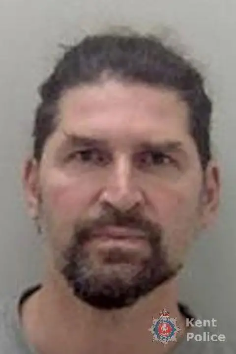 Kent Police a custody image of a man with dark hair and dark beard, wearing a grey t-shirt