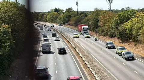 Richard Knights/BBC Police cars by a lorry and black car at the scene of the crash. Traffic is flowing normally on the southbound carriageway.