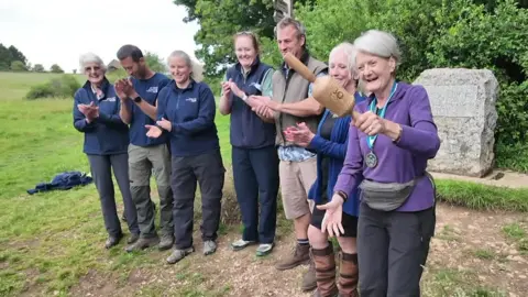 A line of people with a woman holding a wooden baton. They are at the start of the Thames Path.