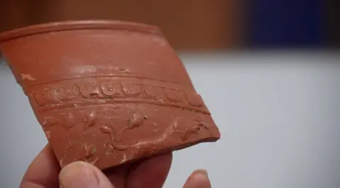 A piece of carved teracotta pottery being held up in someone's hand