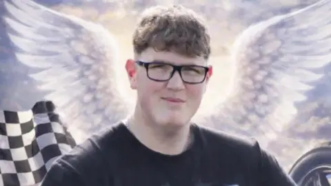 South Yorkshire Police An image of a young man with glasses and short curly brown hair. He is looking at the camera and smiling. Behind him are some animated angel wings, a black and white chequered racing flag and a tyre.