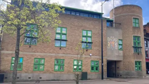 Luton Crown Court: A brown-brick building with green-framed windows. The word "CROWN COURT" are written above the entrance.