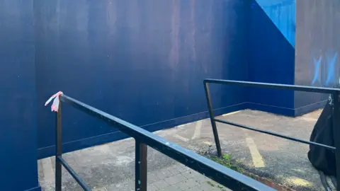 A large wooden wall painted blue, with a disabled access ramp leading from it