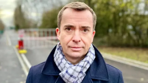 Calum Miller has short brown hair and is wearing a blue coat and grey scarf.