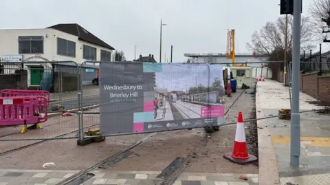 Gurdip Thandi/LDRS Metal fencing at the entrance to a building site. Tram tracks can be seen o the road and a sign says Wednesbury to Brierley Hill.