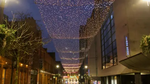 Gold and silver fairy lights suspended high over a road next to the stage door at a theatre