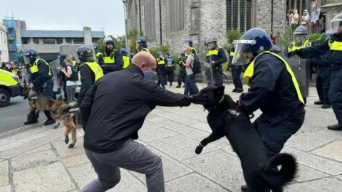 Getty Images A protester and police dog appearing to lunge at each other with police officers in riot gear nearby