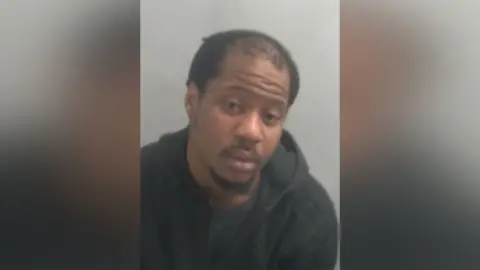 Daniel Odubanjo is looking at the camera in a police custody shot. He has short black hair, thinning at the front. He is wearing a dark-coloured hooded sweatshirt.