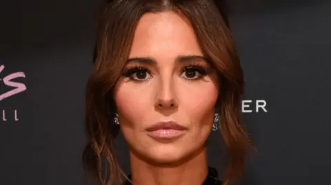 Girls Aloud member Cheryl has a solemn expression and is stood against a black background