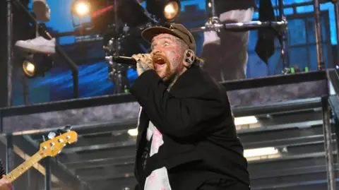 Jim Dyson/Getty Images A male singer wearing a black blazer performing onstage. 