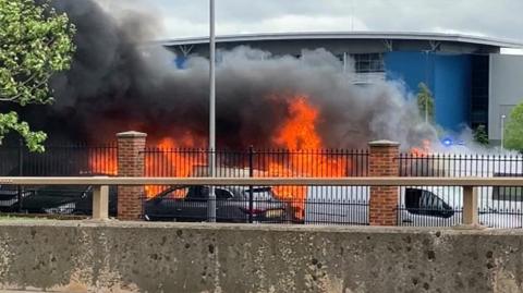Flames and black smoke seen coming from vehicles parked in a car park