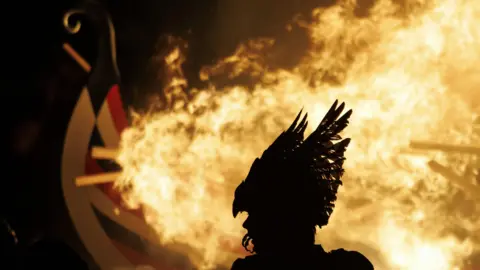 EPA-EFE/REX/Shutterstock Members of the Up Helly Aa festival's 'Jarl Squad' look on as a replica Viking longship is burned during the junior procession in Lerwick, Shetland Islands, Britain, 28 January 2025.