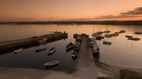 Getty Images A sunset shot of lots of boats in a harbour which has a narrow entrance but widens out 