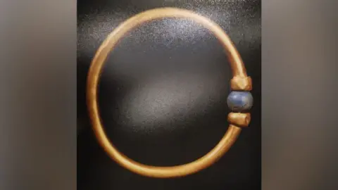 Egyptian Ministry of Tourism and Antiquities The Bracelet is gold and adorned with a blue, round bead.