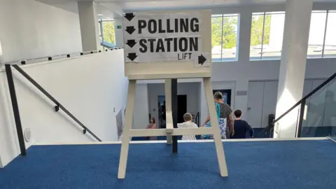 Polling station sign at the front of a staircase in a white painted building.