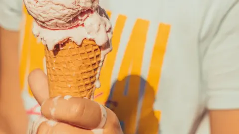 A hand holding an ice cream cone. The ice cream is melting onto the person's hand. 