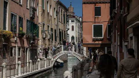 Getty Images People walk on a footbridge in the Dorsoduro district on April 04, 2026 in Venice, Italy. 