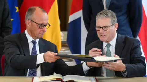 German Chancellor Friedrich Merz (L) and British Prime Minister Keir Starmer (R) exchange documents during the signing of the German-UK Friendship Treaty at the Victoria and Albert Museum