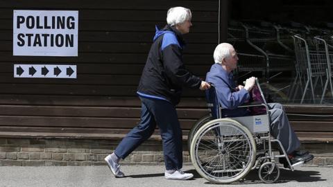 A man in a wheelchair being pushed towards into a polling station