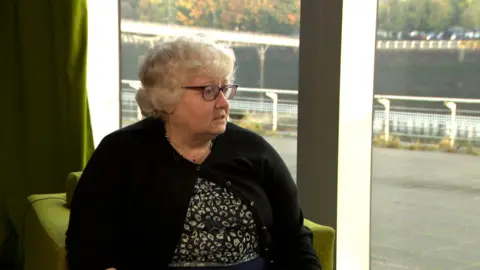 Laura Schosloff wears a flowery apical  and achromatic  cardigan portion    sitting successful  an bureau   with the River Clyde successful  the background