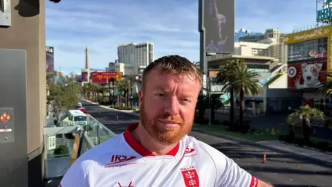 Richard Major Richard Major stands by a road in Las Vegas. He has red hair and beard and is wearing a white HKR shirt 